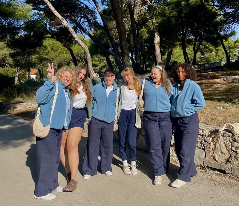 Six Virgin Island contributors in matching blue fleeces, arms around each other under the trees